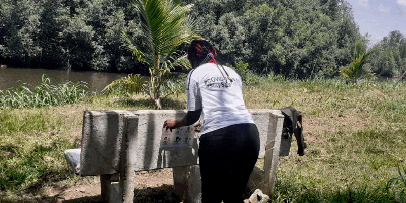 A woman attaches a Covid-19 awareness poster to a bench in Cameroon.