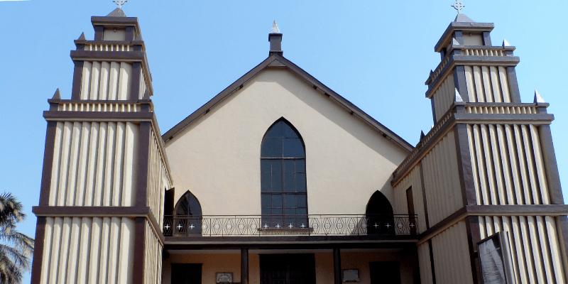 A church, with a palm tree pictured to the left, on a sunny day