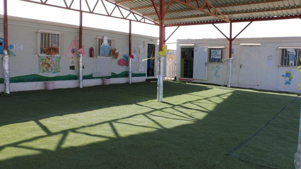 Two builings decorated with images of Smurfs. A roofed courtyard protects a lawn from the sun. 